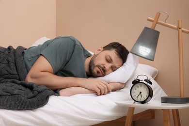 Photo of Man sleeping in bed and alarm clock on nightstand at home