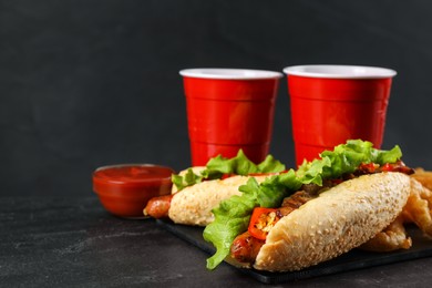 Photo of Tasty hot dogs, fried onion rings and refreshing drink on black table, space for text. Fast food