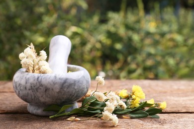 Photo of Mortar with pestle, dry flowers and ears of wheat on wooden table outdoors