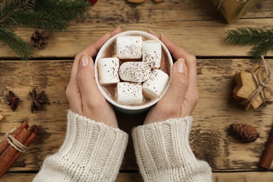 Photo of Woman with cup of delicious marshmallow cocoa at wooden table, top view