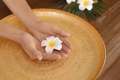 Photo of Woman soaking her hands in bowl with water and flowers on table, closeup. Spa treatment
