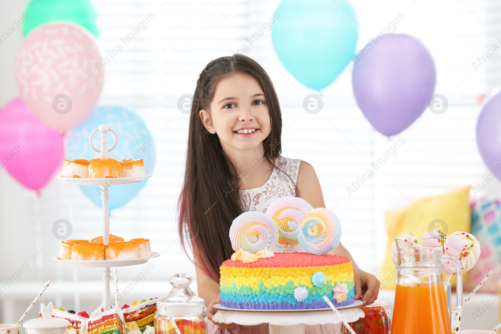 Photo of Happy girl at table with treats in room decorated for birthday party