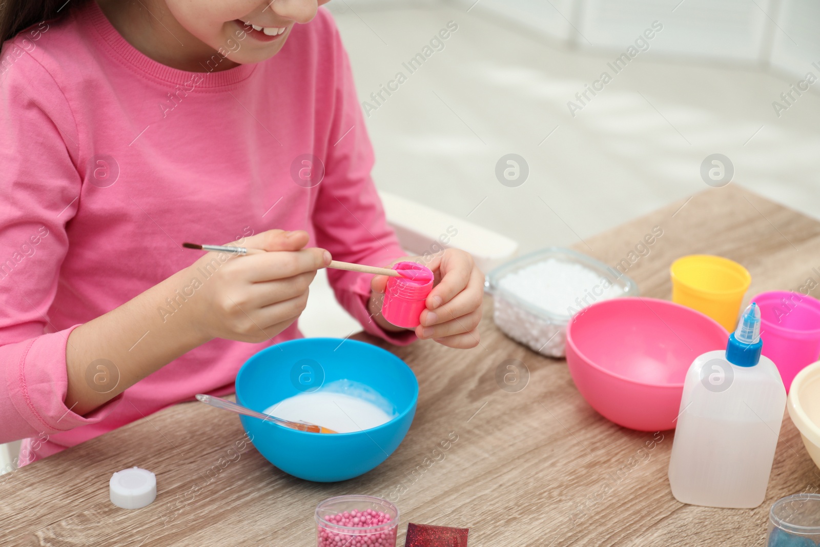 Photo of Little girl making homemade slime toy at table, closeup