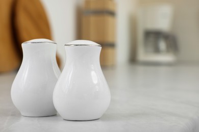 Ceramic salt and pepper shakers on white table in kitchen. Space for text