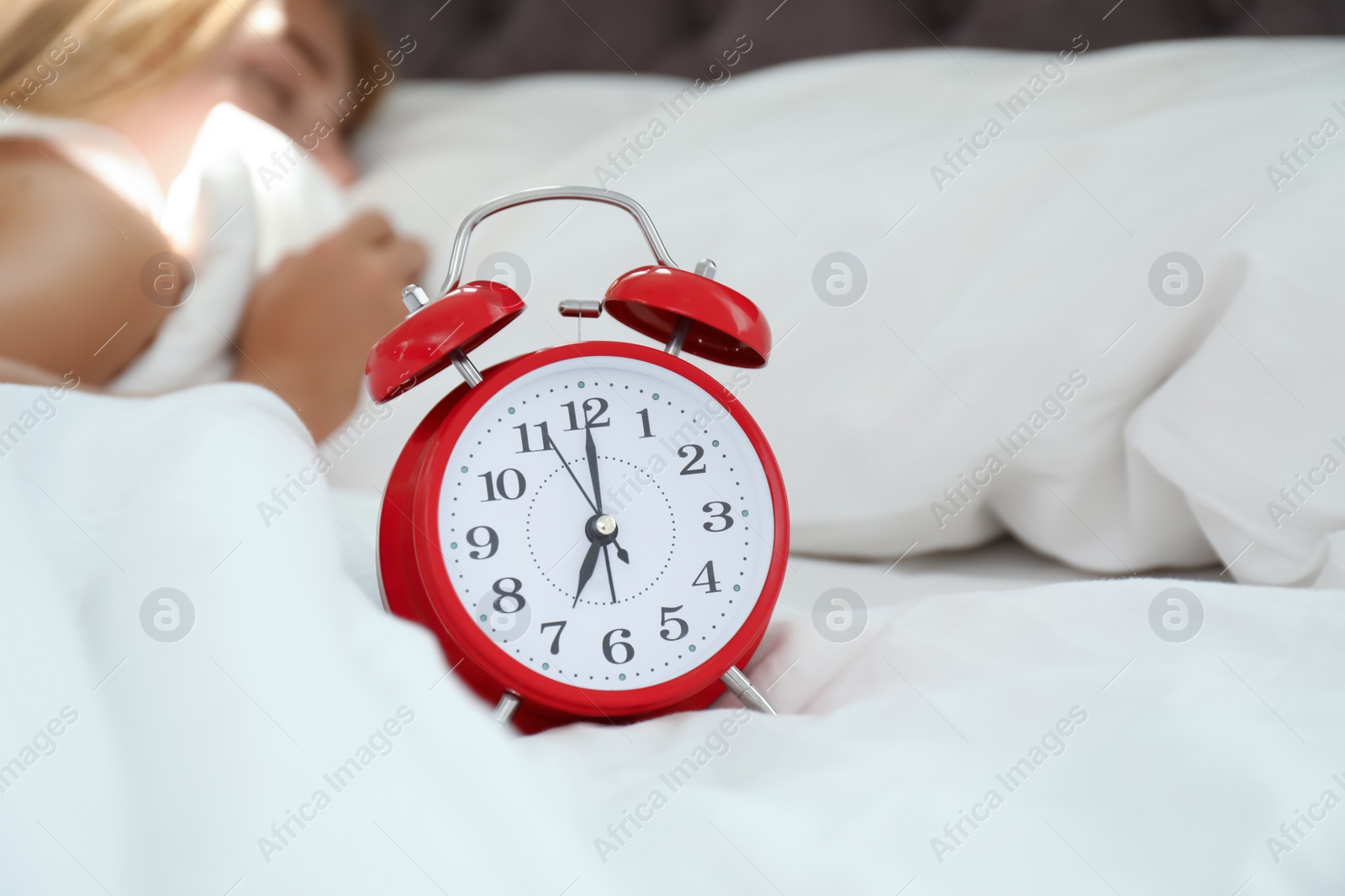 Photo of Analog alarm clock and sleepy woman in bed. Time of day