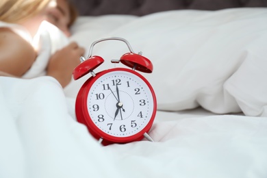 Analog alarm clock and sleepy woman in bed. Time of day