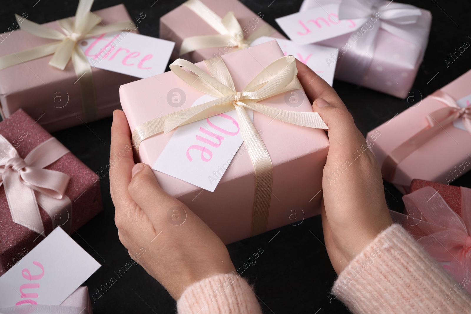 Photo of Woman with gift box at black table, closeup. Advent calendar