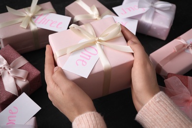 Woman with gift box at black table, closeup. Advent calendar