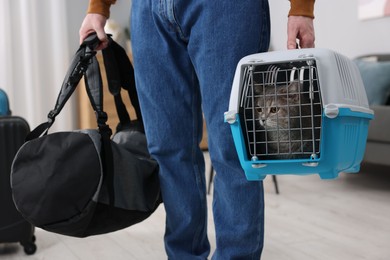 Travel with pet. Man holding carrier with cute cat and bag at home, closeup