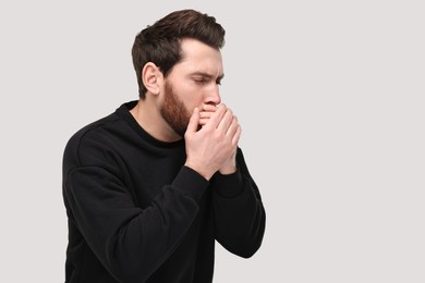 Sick man coughing on light grey background, space for text. Cold symptoms