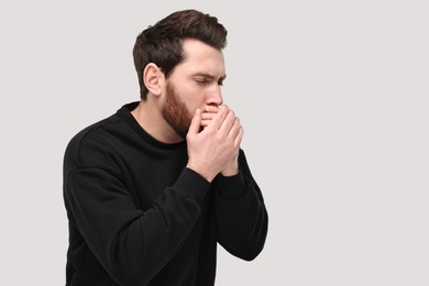 Photo of Sick man coughing on light grey background, space for text. Cold symptoms