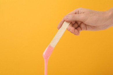 Woman holding spatula with hot depilatory wax on yellow background, closeup