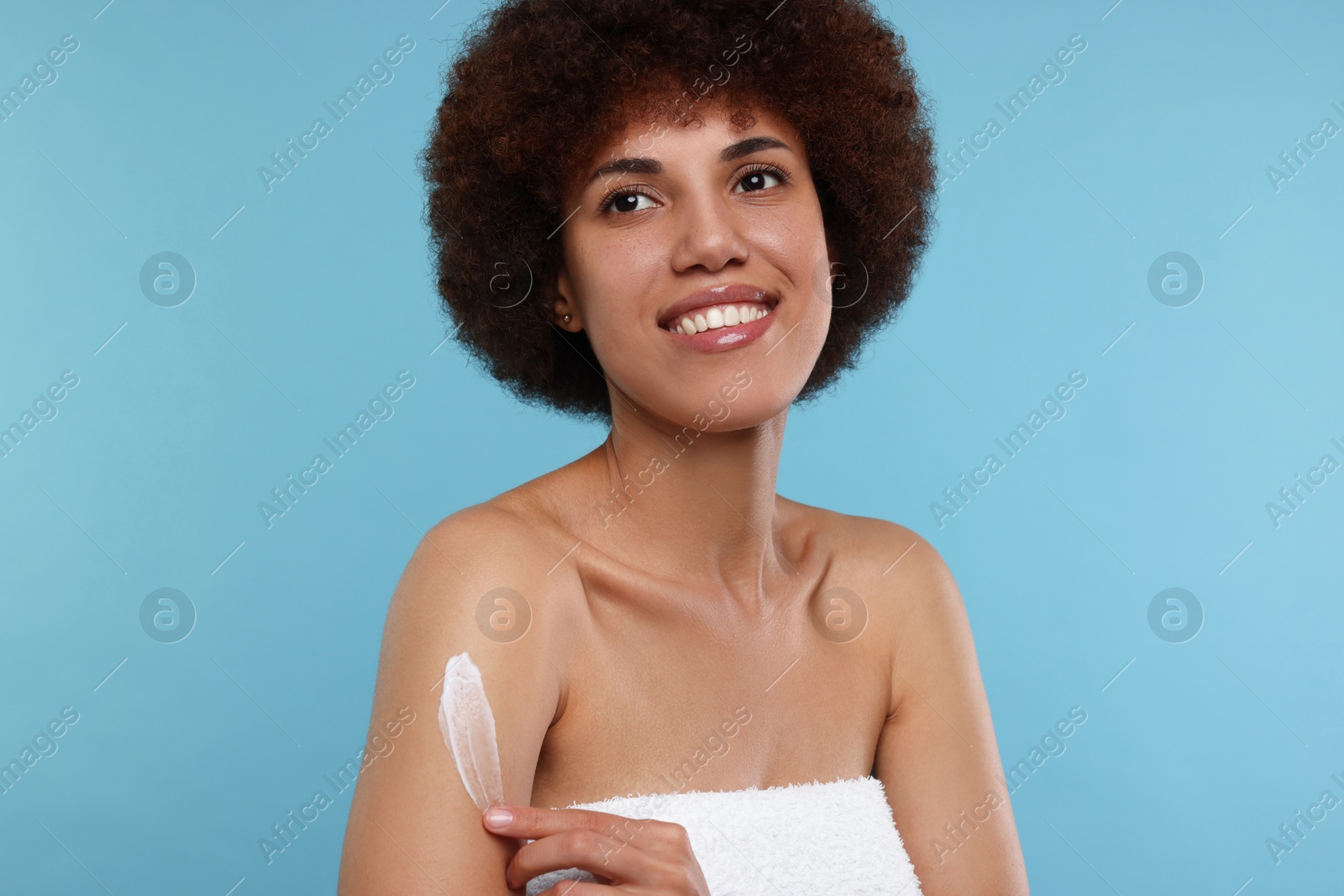 Photo of Beautiful young woman applying body cream onto arm on light blue background