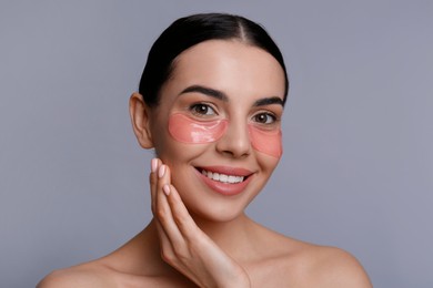 Beautiful young woman with under eye patches on grey background