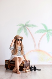 Photo of Adorable little child playing traveler with suitcase indoors