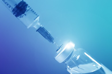 Image of Filling syringe with medicine from vial on blue background, closeup