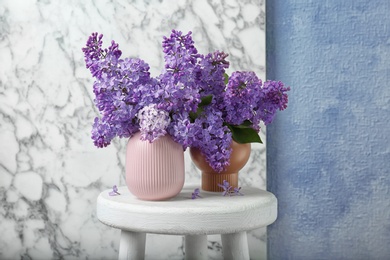 Photo of Vases with beautiful blossoming lilac on table against wall. Spring flowers