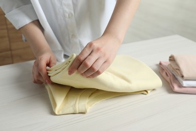 Photo of Woman folding clothes at white wooden table indoors, closeup