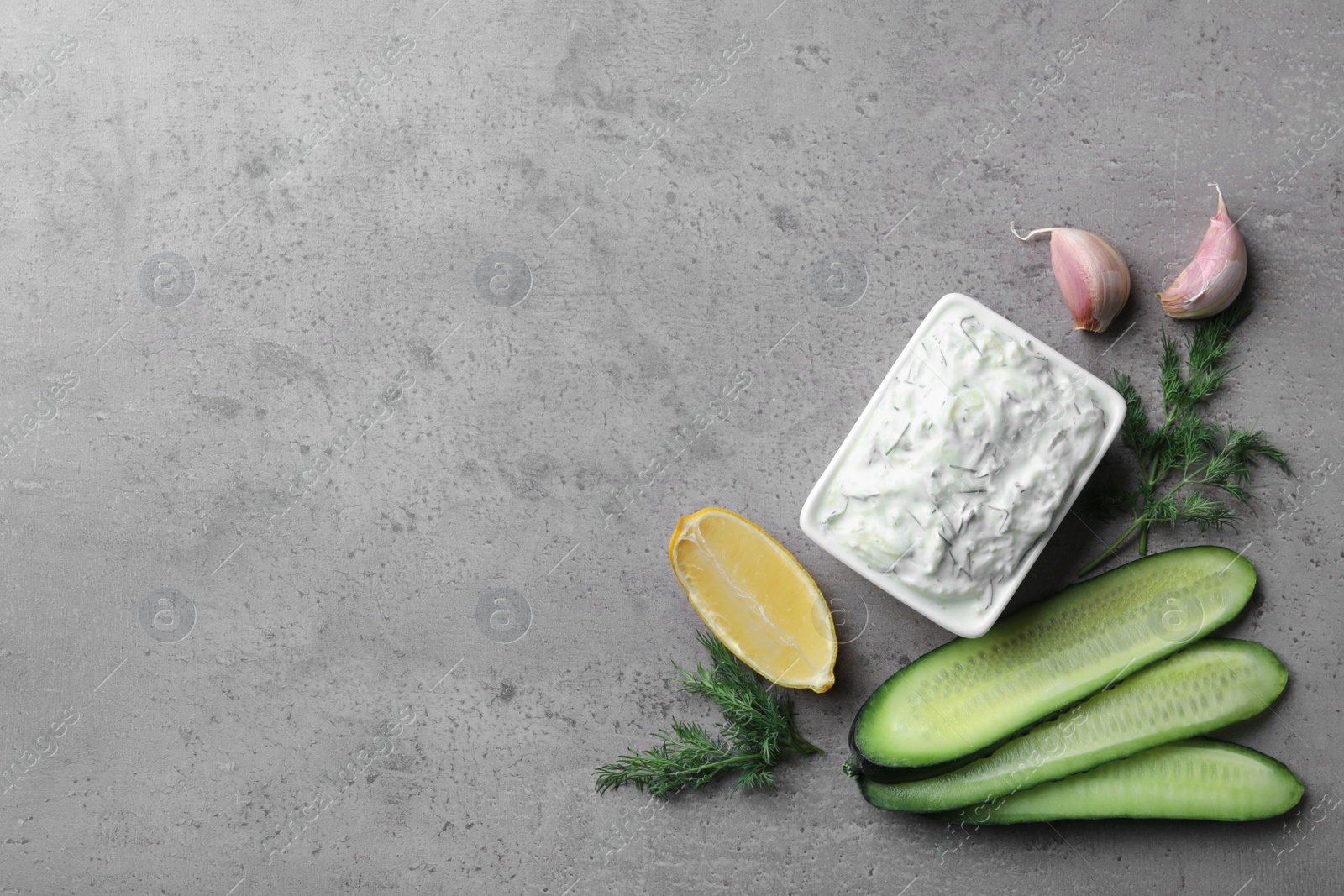 Photo of Bowl of traditional Tzatziki sauce with garlic, lemon, cucumber and dill on grey background, top view. Space for text