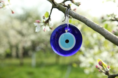Photo of Evil eye amulet hanging on blossoming spring tree outdoors, closeup. Space for text