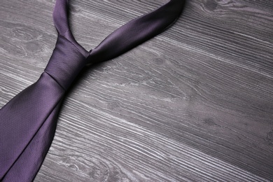 Photo of Stylish purple silk necktie on dark grey wooden table, space for text