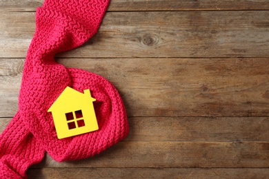 Photo of House model and scarf on wooden background, top view with space for text. Heating efficiency