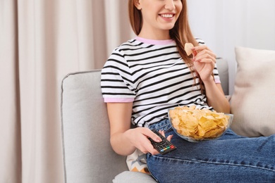 Photo of Woman with bowl of chips on couch, closeup. Watching TV