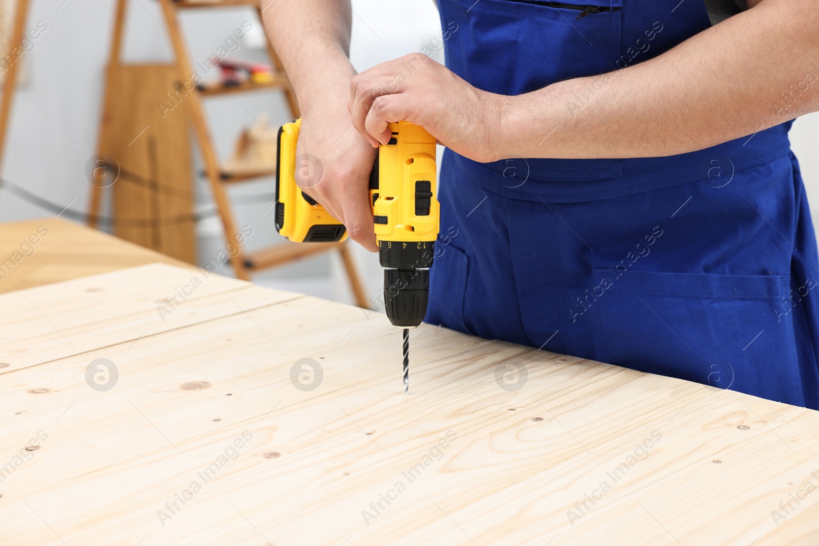 Photo of Young worker using electric drill at table in workshop, closeup