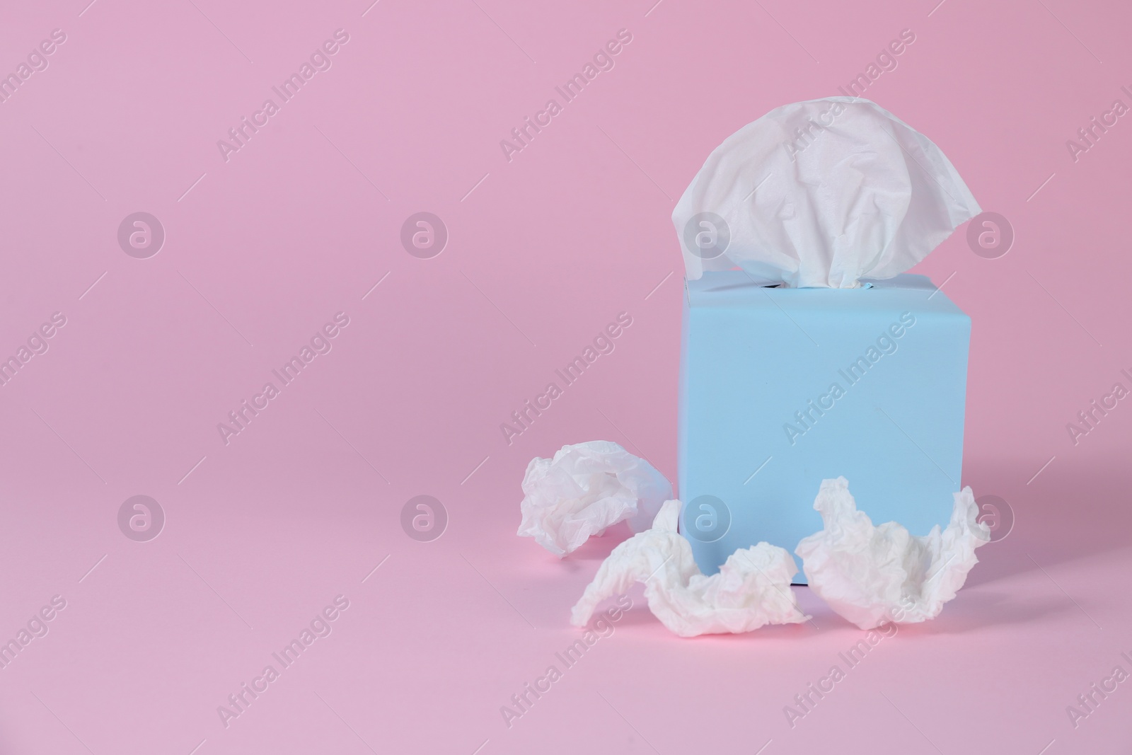 Photo of Box with paper tissues and used crumpled napkins on pink background, space for text