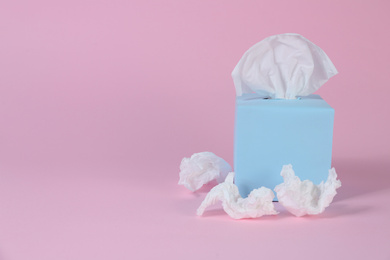 Box with paper tissues and used crumpled napkins on pink background, space for text