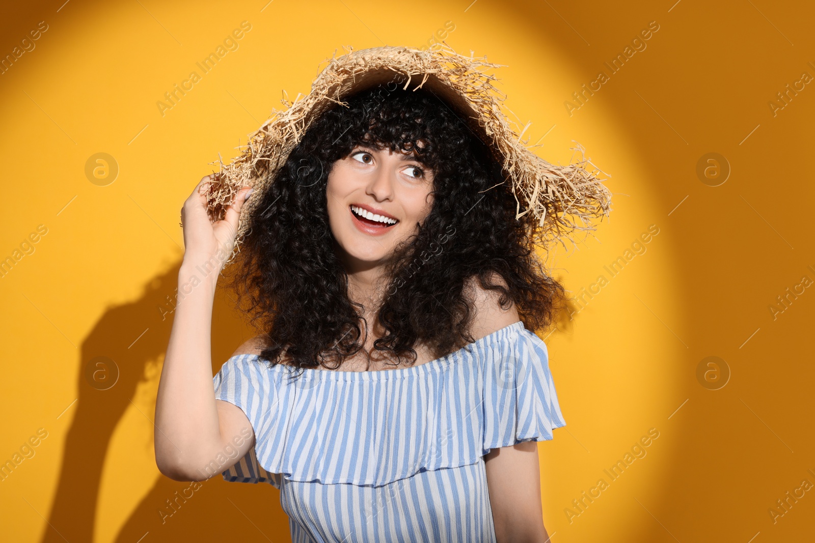 Photo of Beautiful young woman wearing straw hat in sunlight on orange background. Sun protection accessory