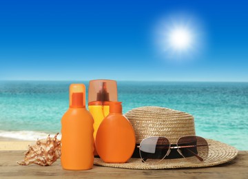 Different bottles of skin sun protection products and beach accessories on wooden table against seascape. Space for design