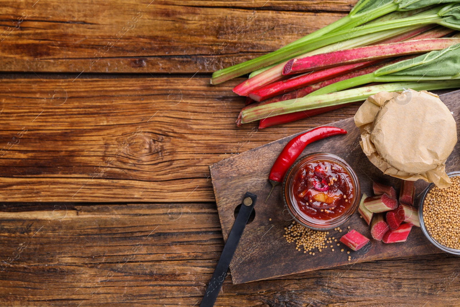 Photo of Tasty rhubarb sauce and ingredients on wooden table, flat lay. Space for text