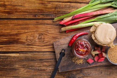 Photo of Tasty rhubarb sauce and ingredients on wooden table, flat lay. Space for text