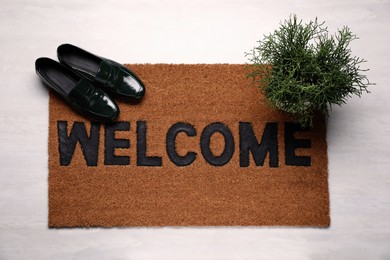 Photo of New clean mat with word WELCOME, shoes and plant on floor, top view