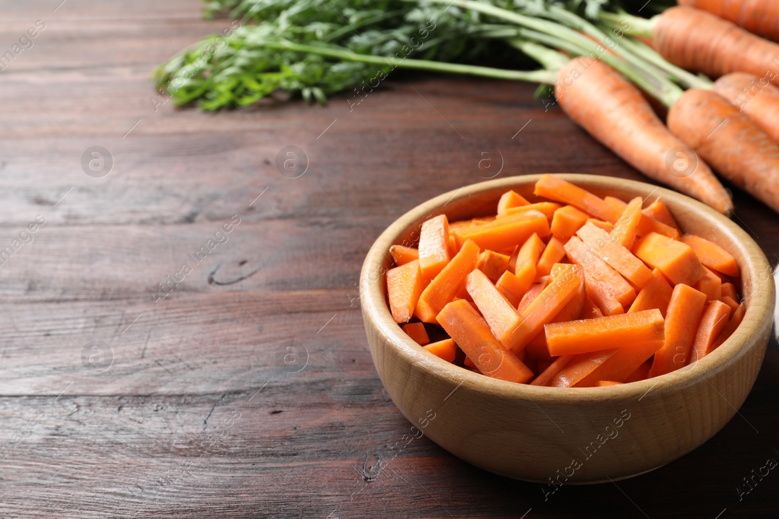 Photo of Cut carrot in bowl on brown wooden table, closeup. Space for text