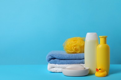 Photo of Baby cosmetic products, bath duck, sponge and towels on light blue background. Space for text