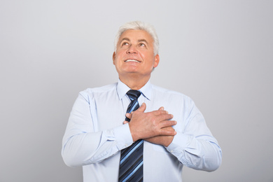 Grateful senior man with hands on chest against light grey background