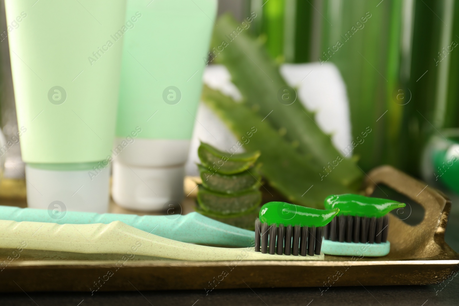 Photo of Aloe vera toothpaste, brushes, green leaves and care products on grey table, closeup