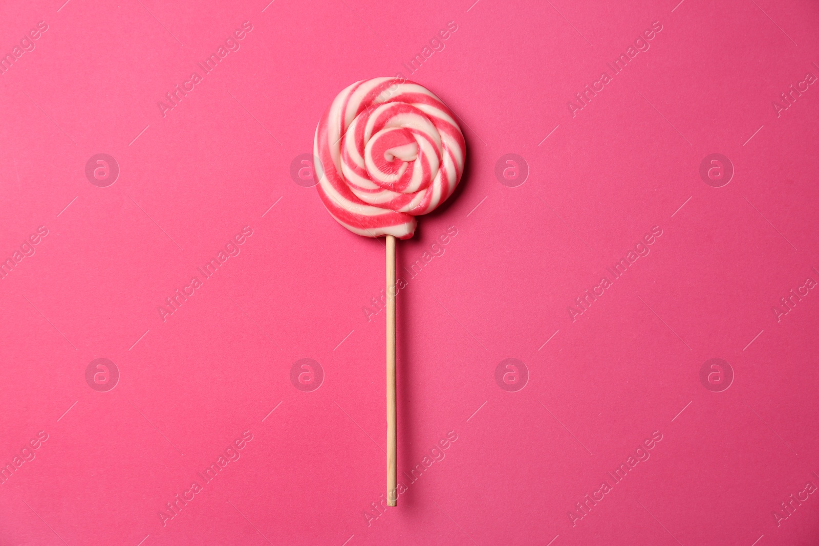 Photo of Stick with tasty sweet lollipop on pink background, top view