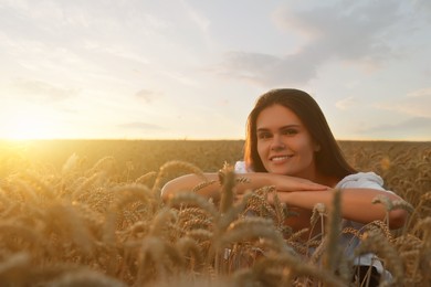 Photo of Beautiful young woman sitting in ripe wheat field at sunset, space for text