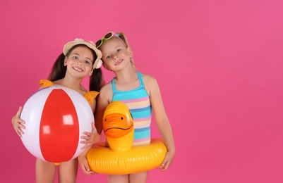 Photo of Cute little children in beachwear with bright inflatable toys on pink background. Space for text