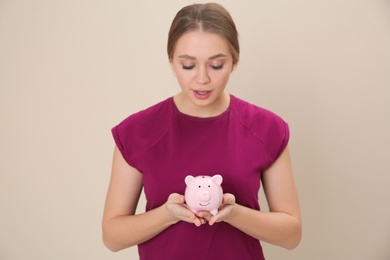 Photo of Young woman with piggy bank on color background. Money saving
