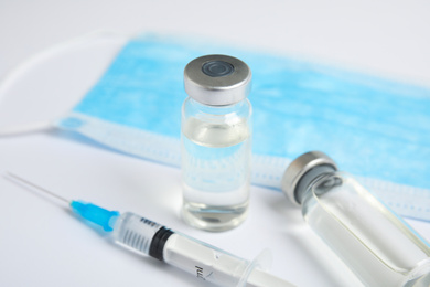 Vials, syringe and surgical mask on light background. Vaccination and immunization