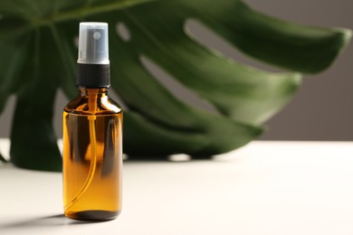 Spray bottle with oil and green leaf on white table, space for text. Natural cosmetics