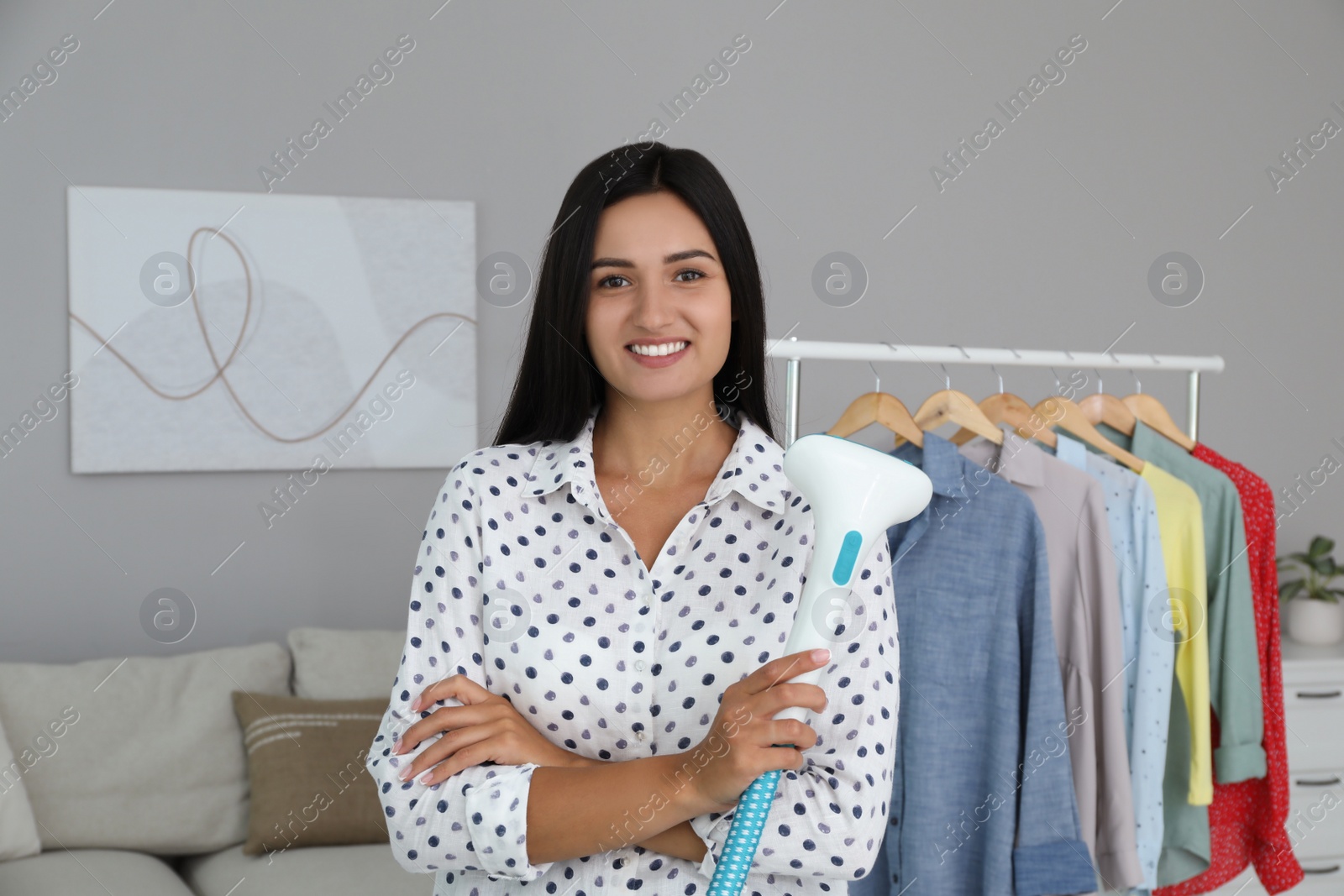 Photo of Happy woman with steam iron near rack of clothes at home