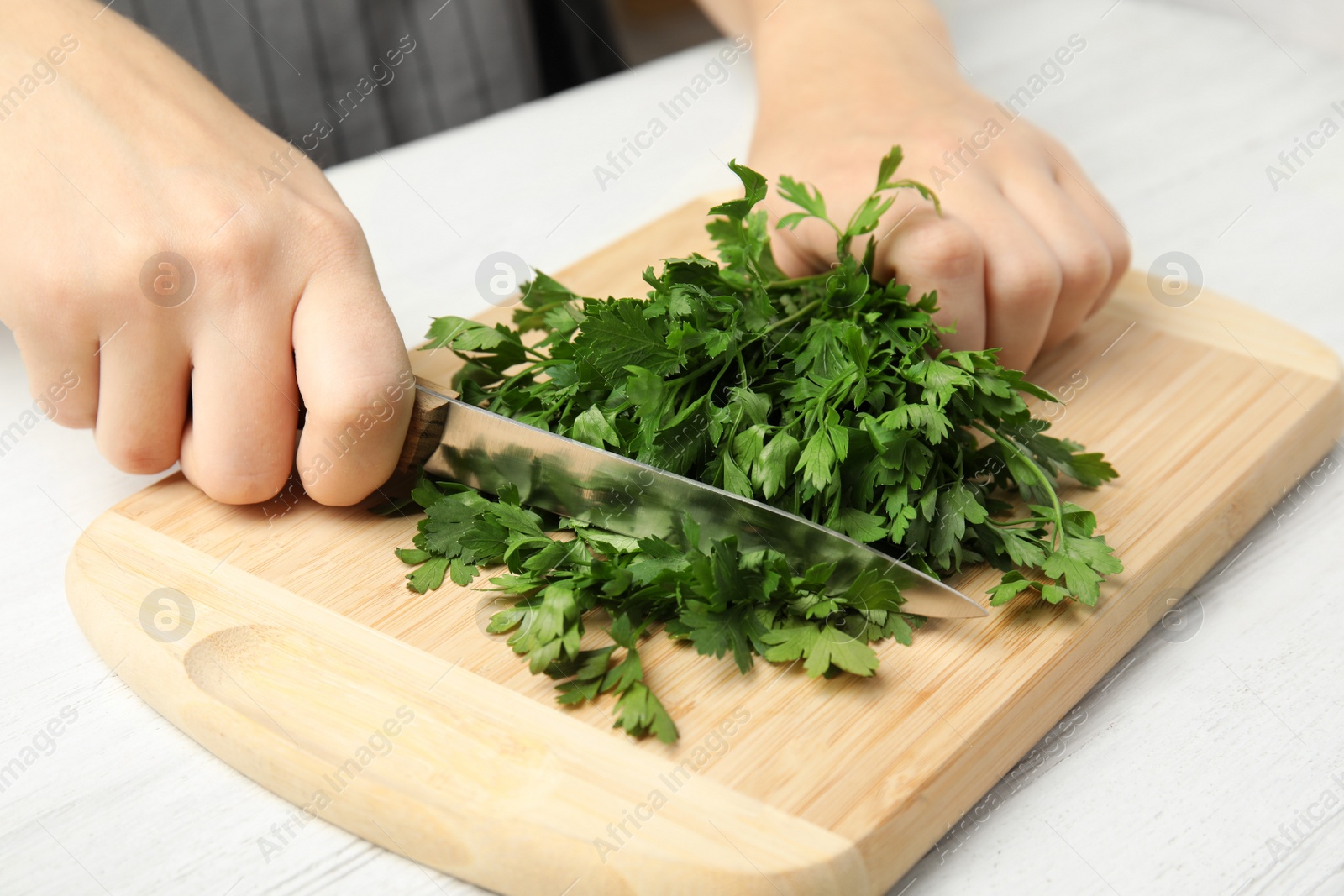 Photo of Woman cutting fresh green parsley on wooden board at table, closeup