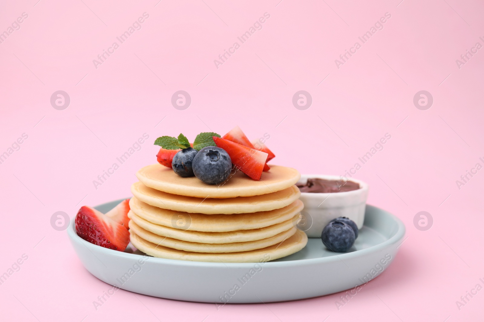 Photo of Delicious pancakes with strawberries, blueberries and chocolate sauce on pink background