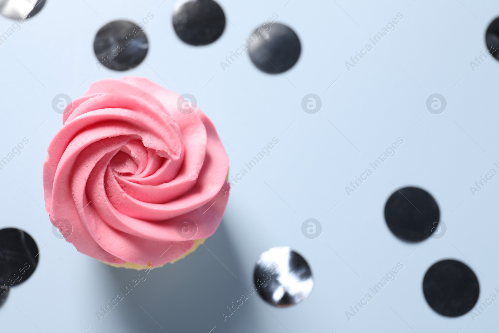 Photo of Delicious cupcake with bright cream and confetti on light background, flat lay