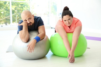 Photo of Tired overweight man and woman resting on fitness balls in gym